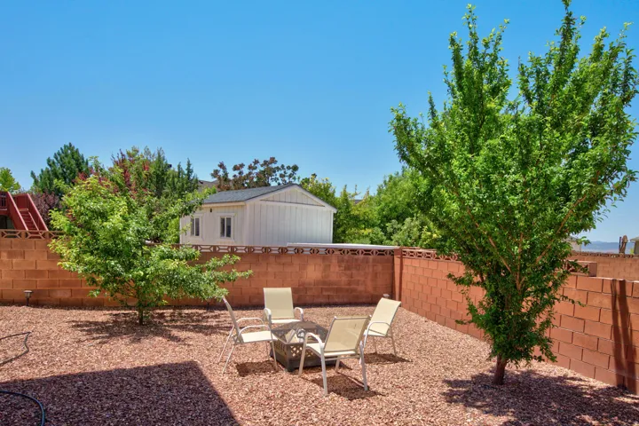Spacious backyard featuring a full block perimeter wall, mature trees, and gravel ground cover