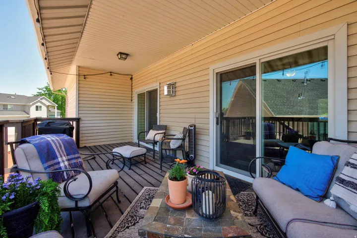 Covered wood-decked patio with light-toned siding, string lighting, and two sliding glass doors