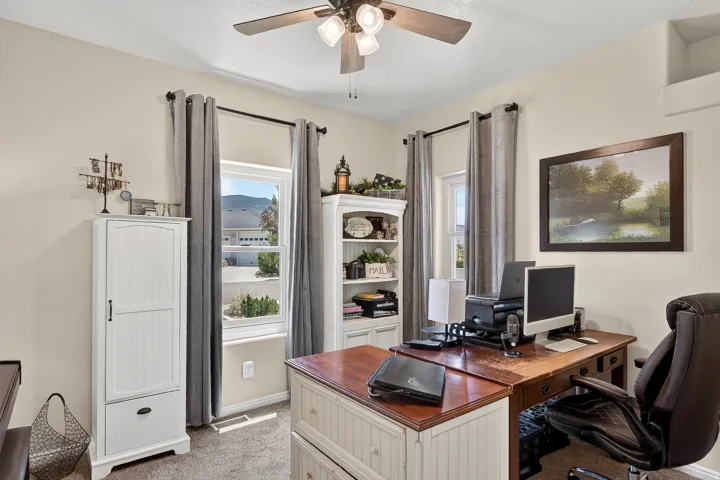 Room featuring neutral wall tones, two windows with dark curtain rods, and a ceiling fan with integrated lighting