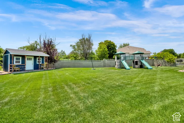 Expansive lawn area featuring a detached storage shed with a covered porch, a stone-accented play structure with dual slides, and a perimeter fence