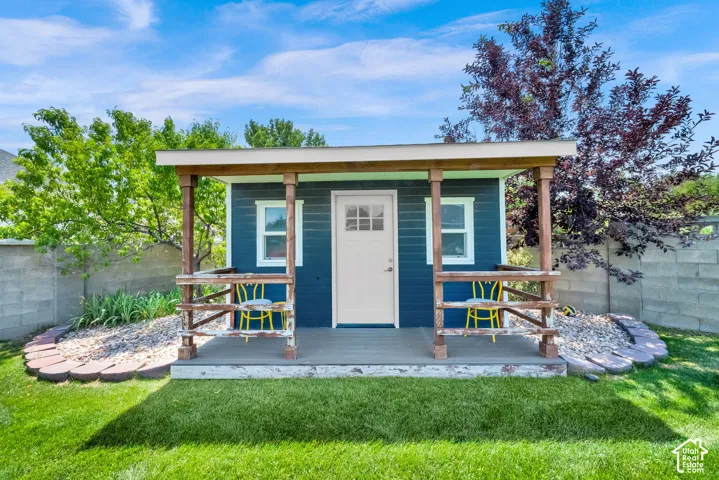 Detached structure with a covered porch featuring a white entry door, two windows, and blue siding