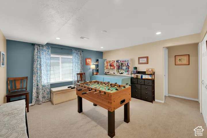 Spacious carpeted room featuring a window with horizontal blinds, recessed lighting, and a built-in shelving unit