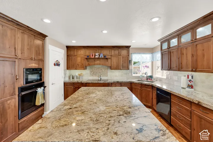 Spacious kitchen featuring a large granite-topped island, extensive wood cabinetry, stainless-steel double oven, and recessed lighting