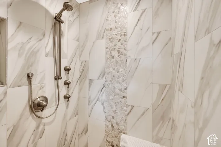Shower stall featuring large format marble-look tile, a pebble tile accent strip, and brushed nickel fixtures including a rainfall shower head and body sprays