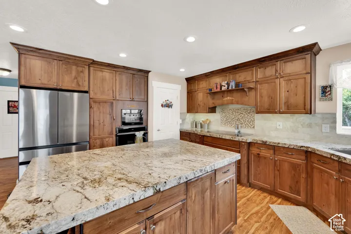 Kitchen featuring a large central island with a stone countertop, extensive wood cabinetry, stainless steel appliances, and wood-finish flooring