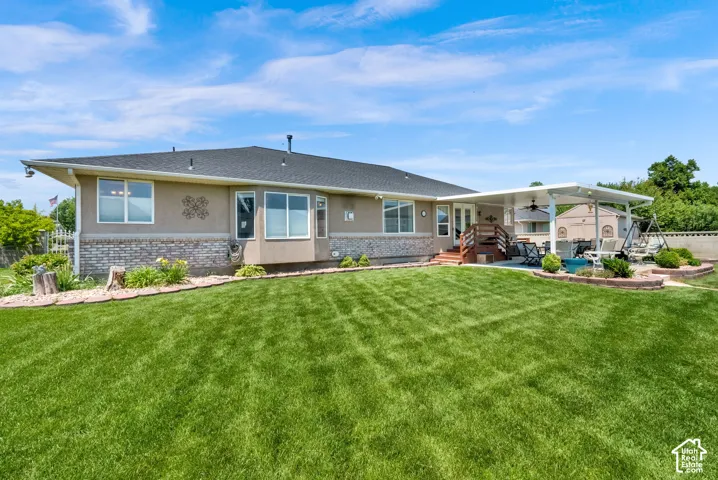 Expansive backyard featuring a manicured lawn, a covered patio structure, and a raised deck with wood railings
