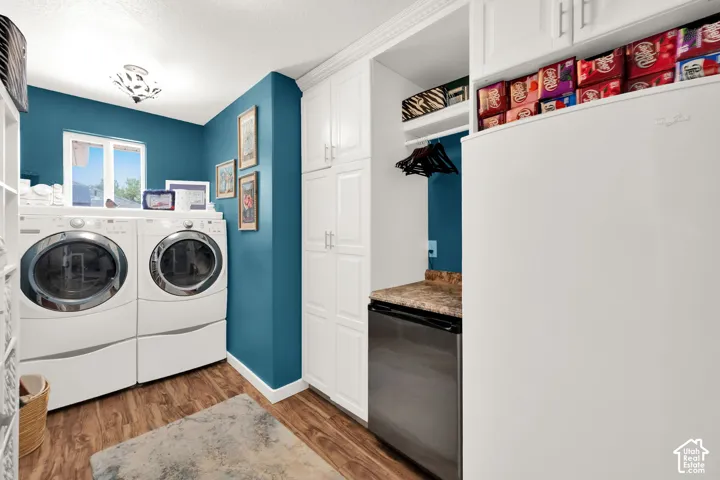 Dedicated laundry area featuring wood-finish flooring, white built-in cabinetry, a built-in hanging rod, and a window for natural light