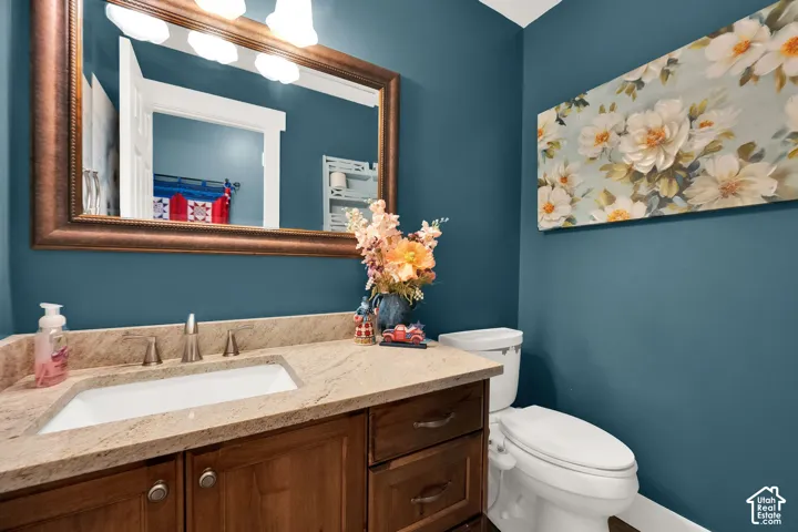 Bathroom vanity featuring a light-toned stone countertop with an undermount sink, a bronze-finish framed mirror with attached overhead lighting, and rich wood-finish cabinetry