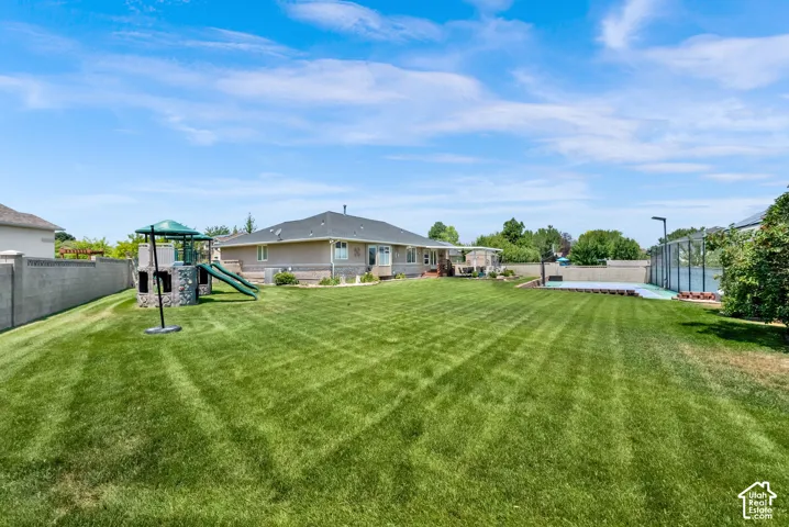 Expansive backyard featuring a lush lawn, a dedicated play structure with slides, a tennis court, and a perimeter fence