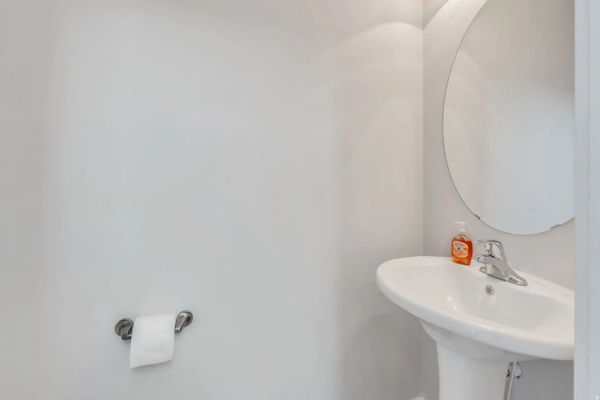 Pedestal sink with chrome faucet, complemented by a round wall-mounted mirror