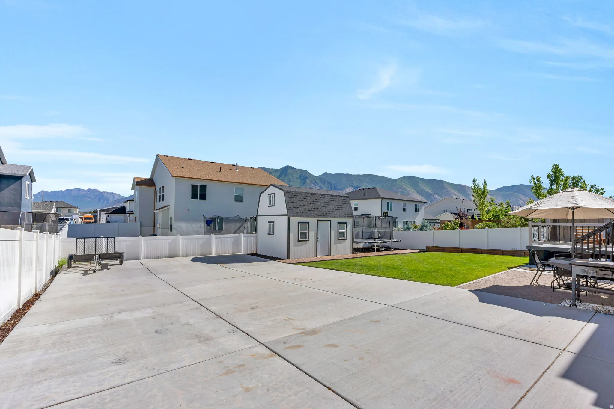 Expansive backyard featuring a large concrete patio, a detached storage shed, a manicured lawn, and white vinyl fencing