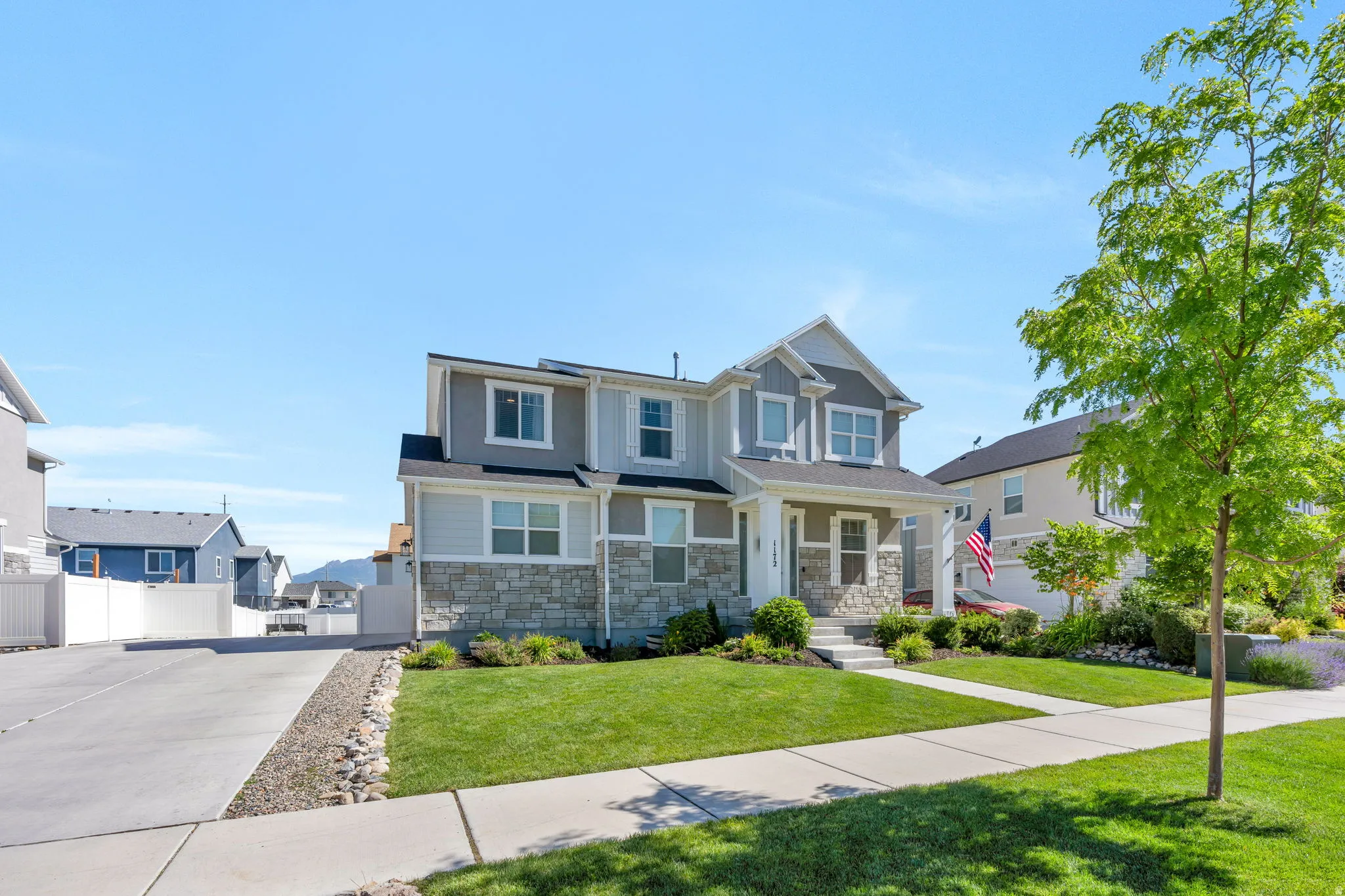 Two-story residence featuring a covered entry, stone and siding facade, concrete driveway, and a manicured lawn with established landscaping