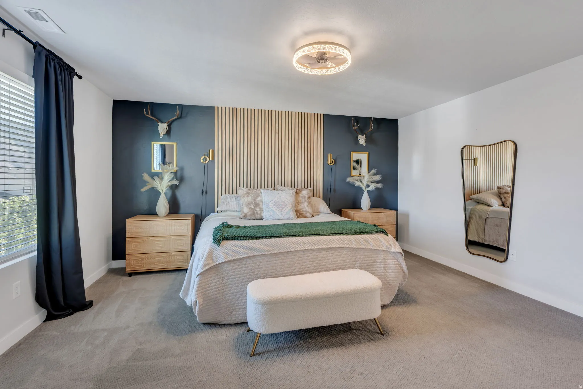 Bedroom featuring a vertical wood slat accent wall, deep blue painted wall, wall-mounted sconces, and a ceiling-mounted light fixture with fan