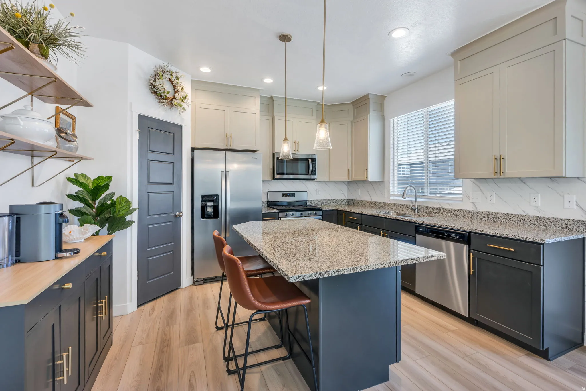 Modern kitchen featuring an island with a granite countertop, light wood-finish flooring, two-tone cabinetry, stainless steel appliances, and a window with blinds