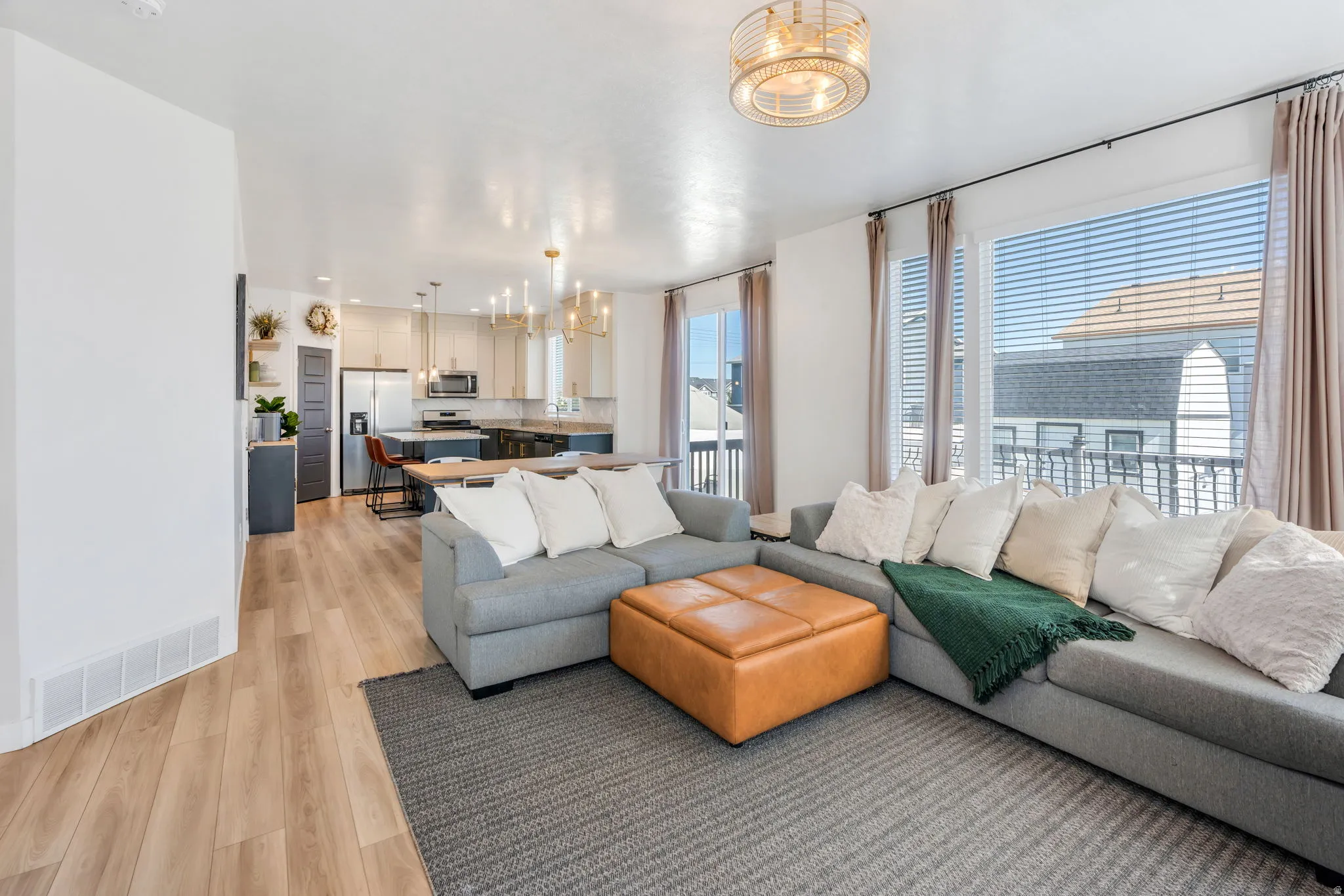 Open-concept living space featuring wood-finish flooring, a contemporary ceiling light fixture, and large windows with blinds