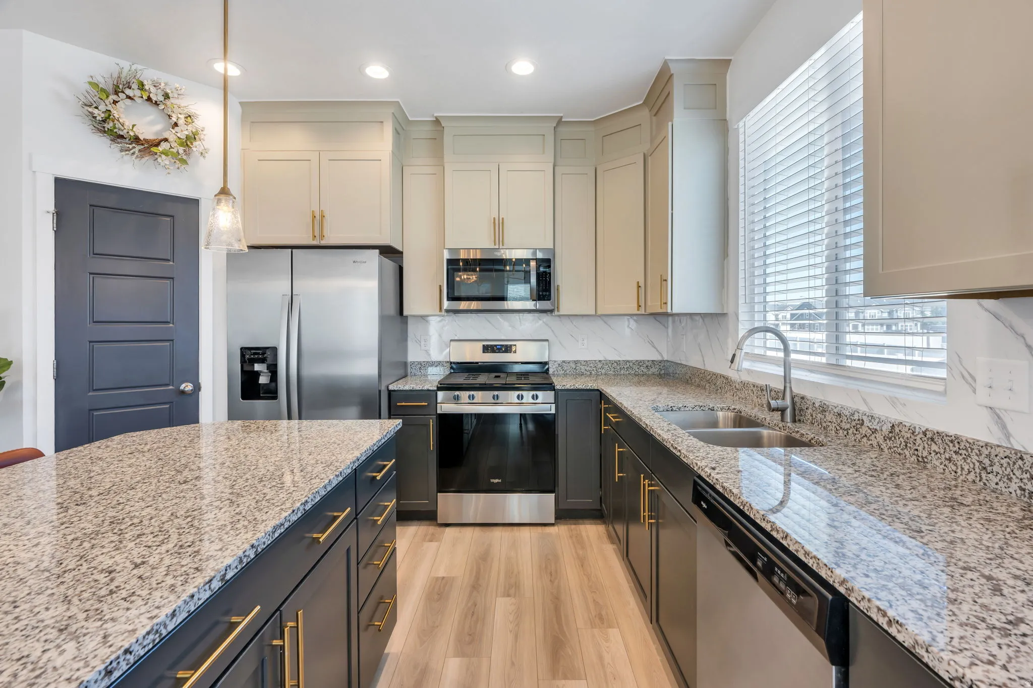 Modern kitchen featuring an expansive island with granite-style countertop, stainless steel appliances, two-tone cabinetry, wood-finish flooring, and a stone-look backsplash