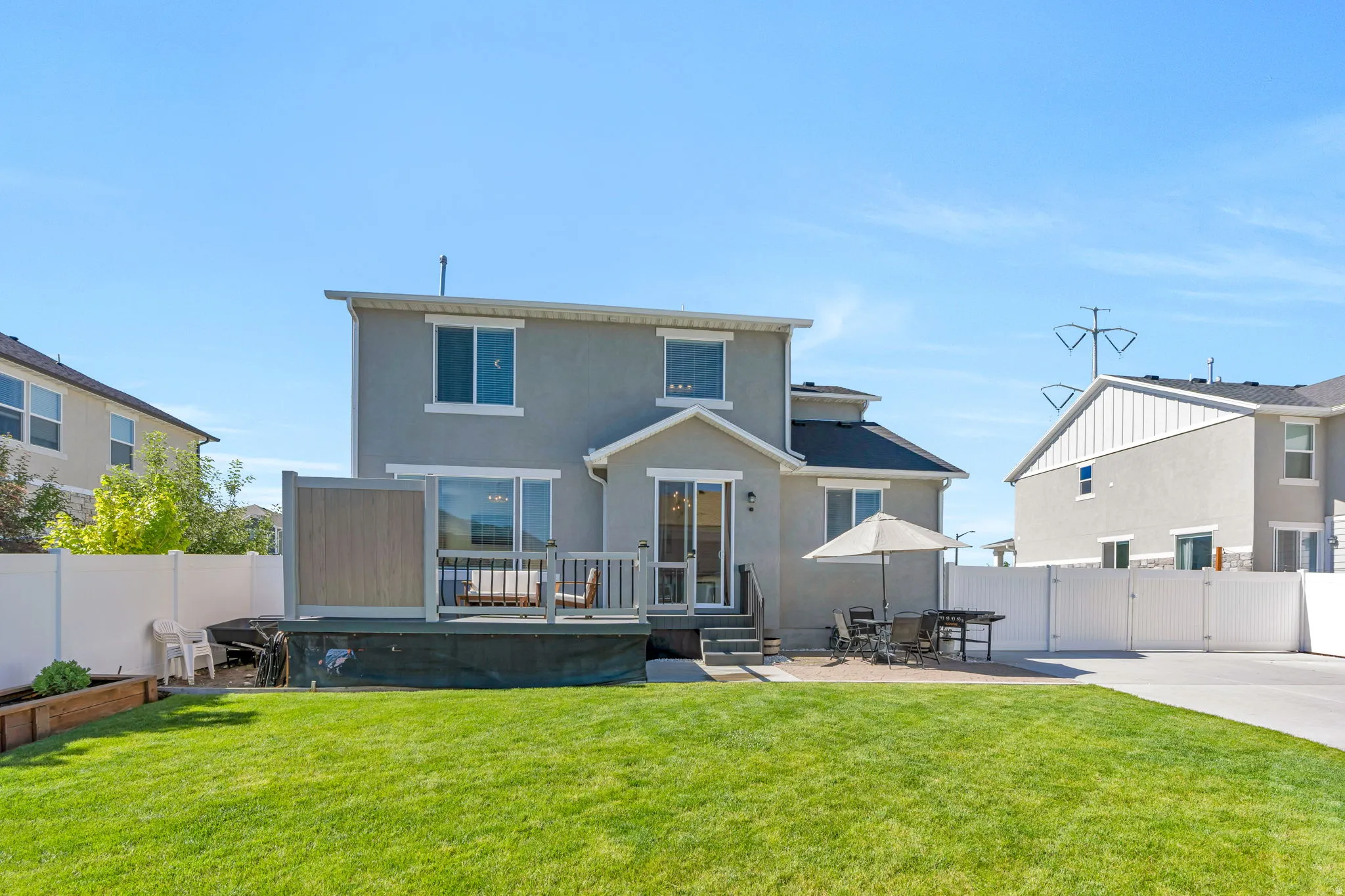 Expansive backyard featuring a manicured lawn, a raised wood deck, and a concrete patio