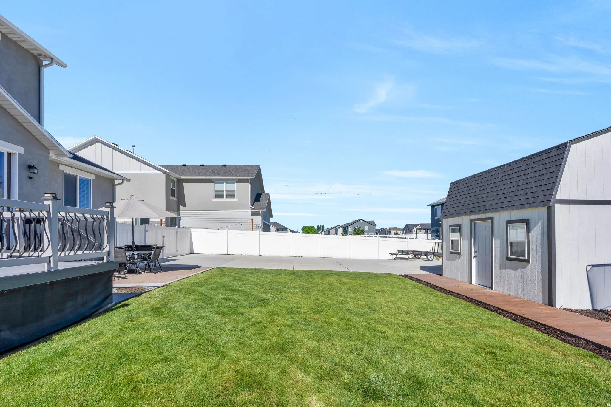 Expansive backyard featuring a manicured lawn, a white vinyl privacy fence, a detached storage shed with a gambrel roof, and a wood-finish pathway