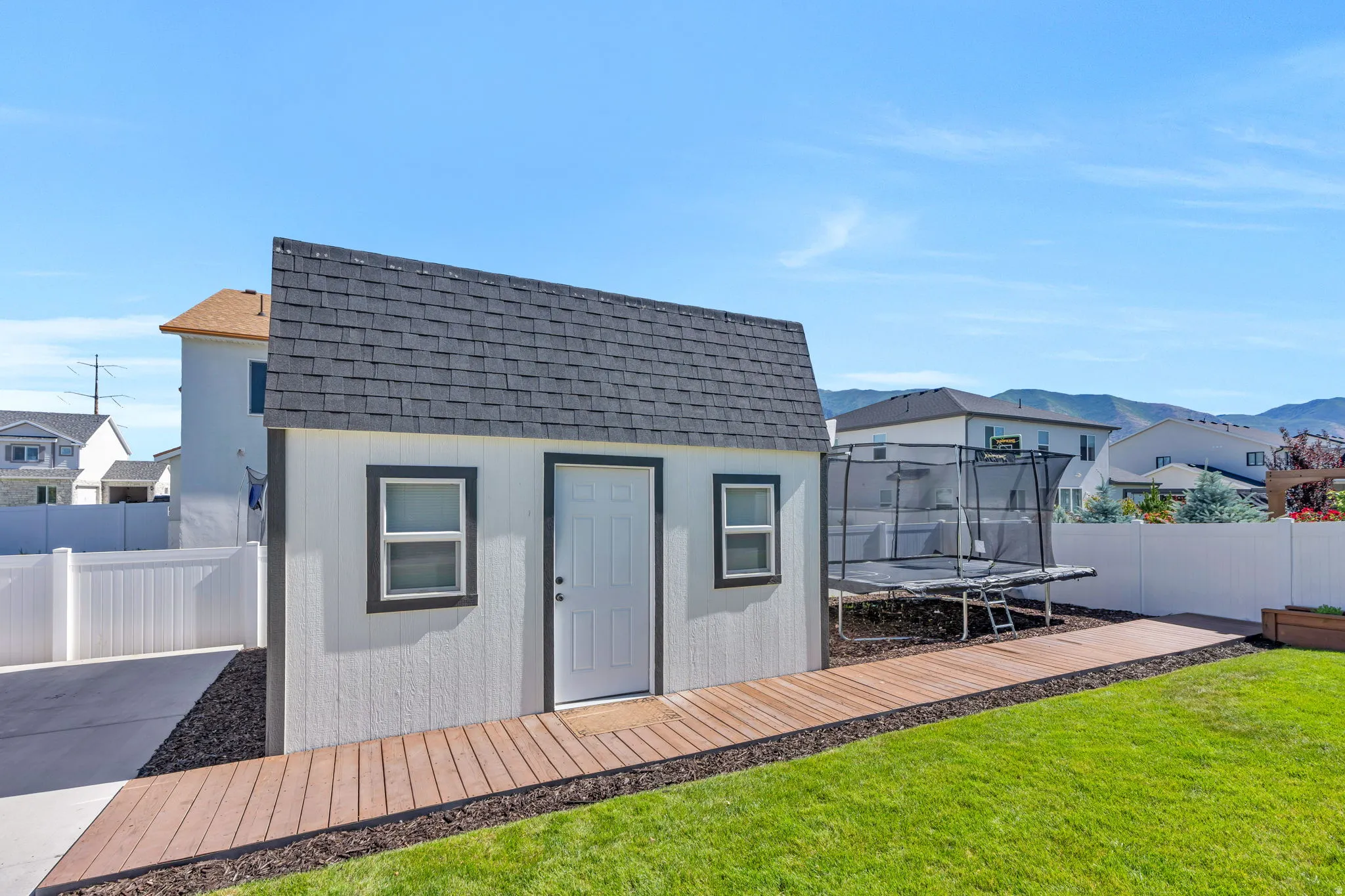 Detached shed with white siding and dark shingle roof, featuring a white entry door and a window with dark trim