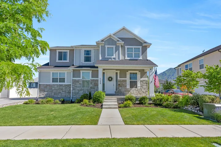 Two-story home with a stone and siding facade, featuring a covered front porch and a manicured front lawn