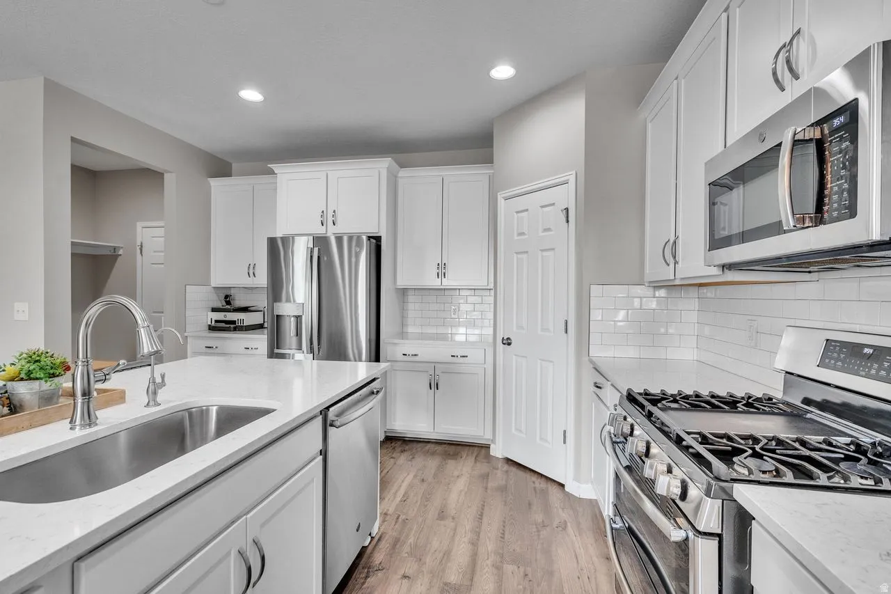 Contemporary kitchen featuring white cabinetry, stainless steel appliances, a gas range, a large kitchen island with an undermount sink, and wood-finish flooring