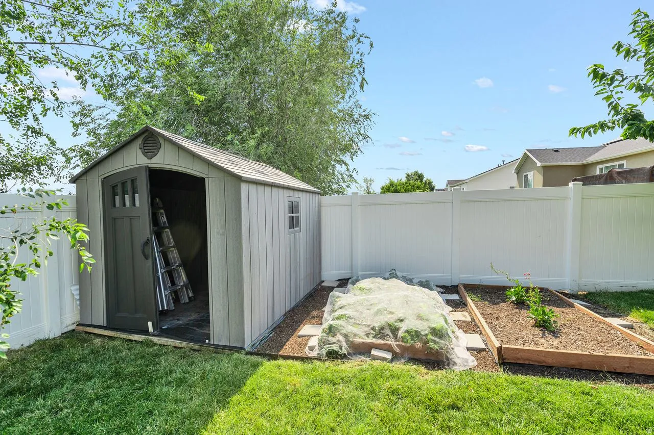 Backyard featuring a shed with a single arched door and side window, white vinyl fencing, and two raised garden beds