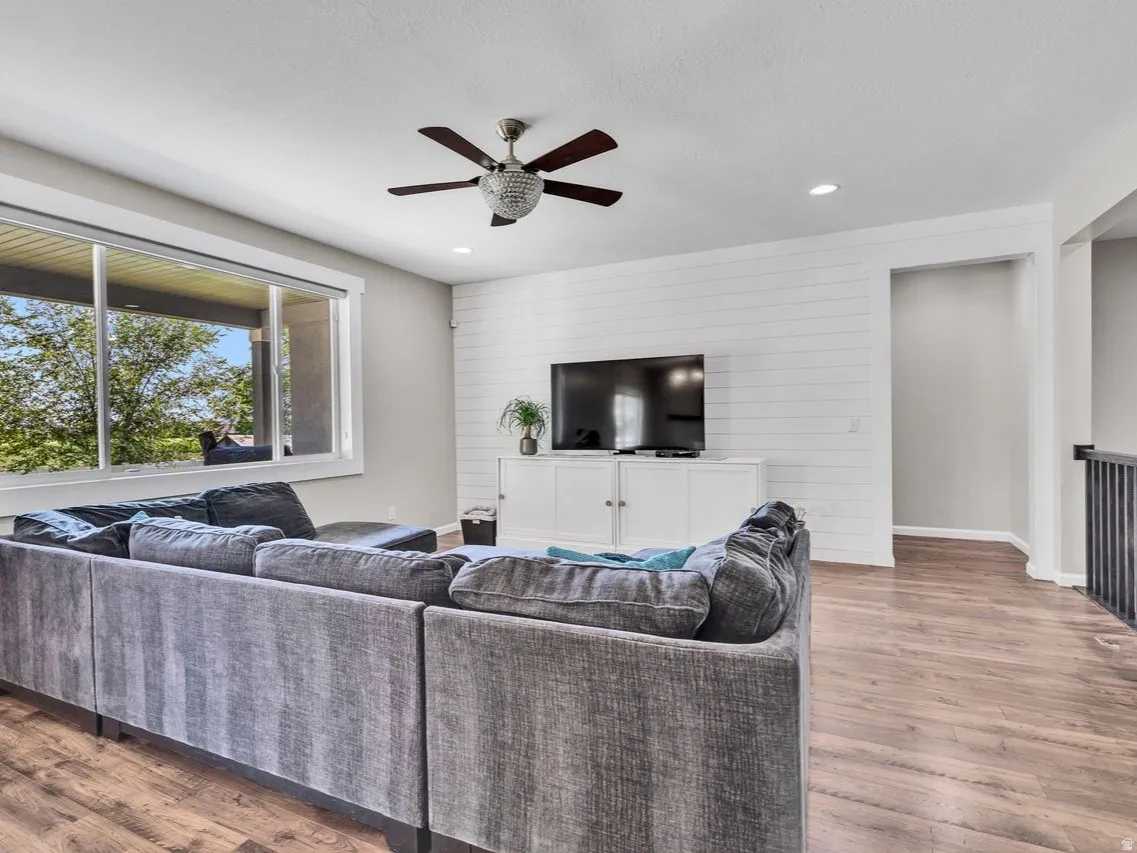 Open-concept living space with wood-finish flooring, a contemporary ceiling fan, recessed lighting, and a shiplap accent wall