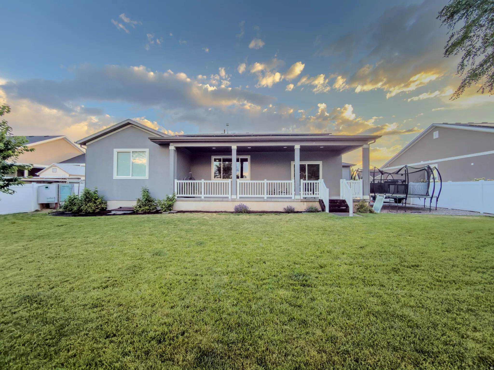 Expansive backyard featuring a manicured lawn, a covered patio, and a white picket railing