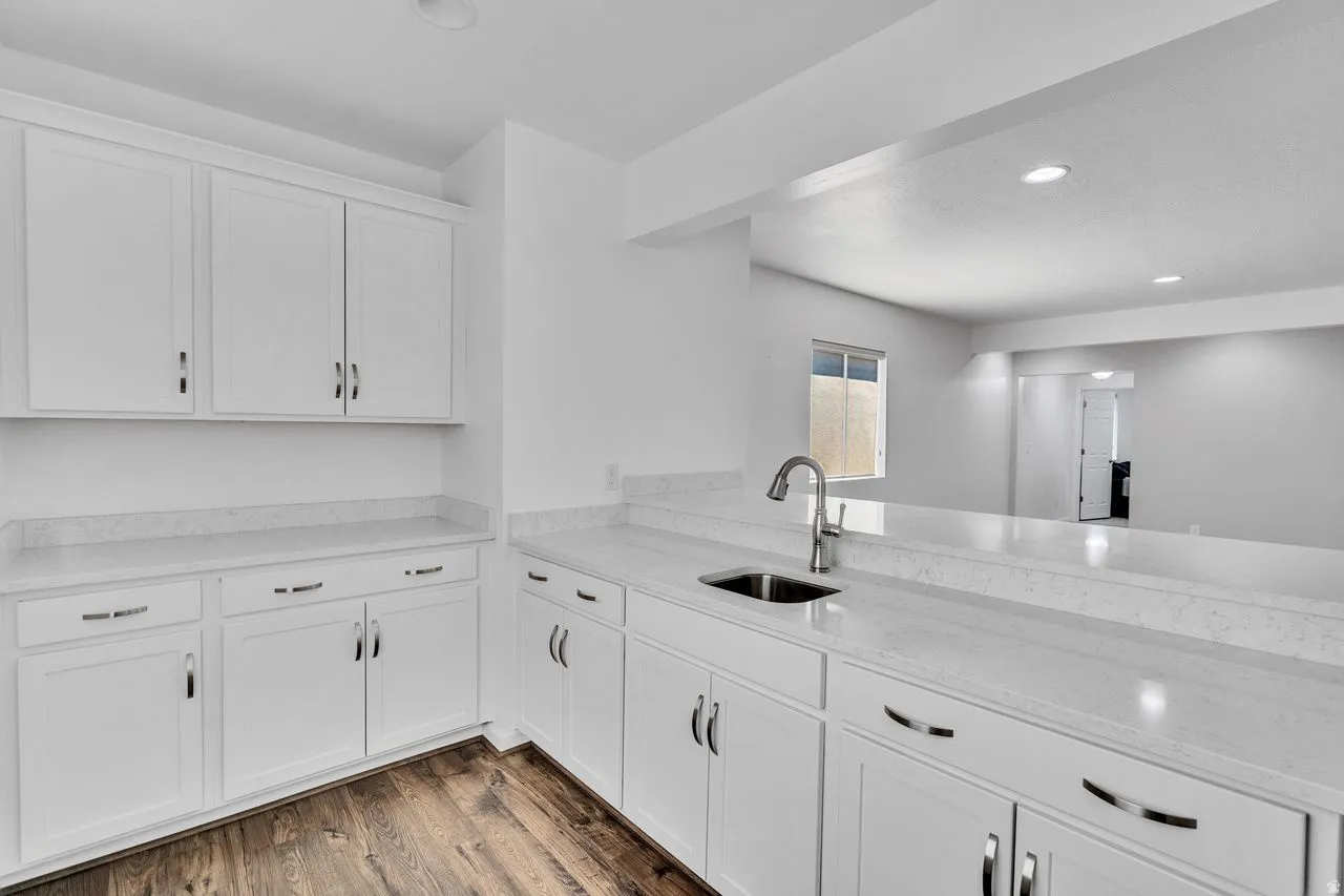 Contemporary kitchen featuring white shaker cabinetry, light-toned countertops, a stainless steel sink with a high-arch faucet, recessed lighting, and wood-finish flooring