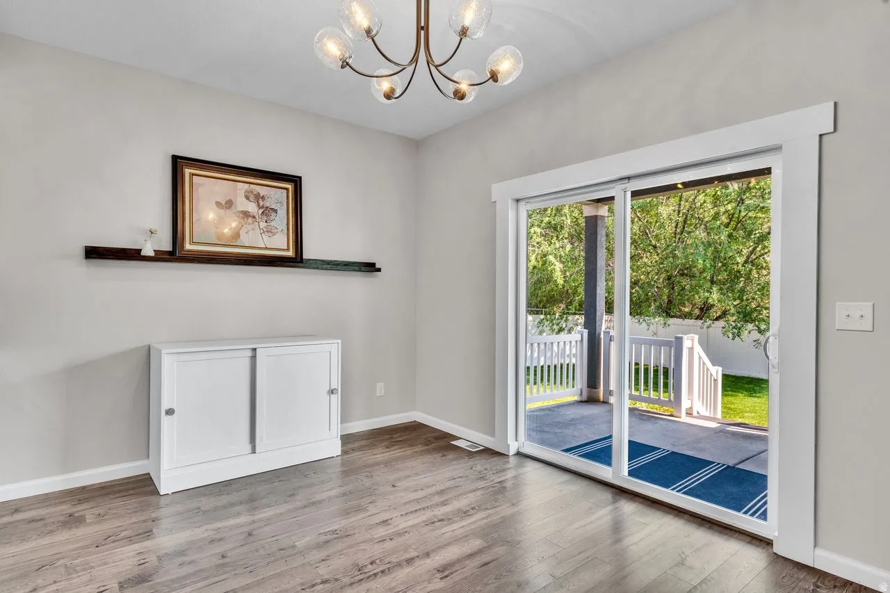 Sliding glass patio door with white trim, wood-finish flooring, and a contemporary chandelier