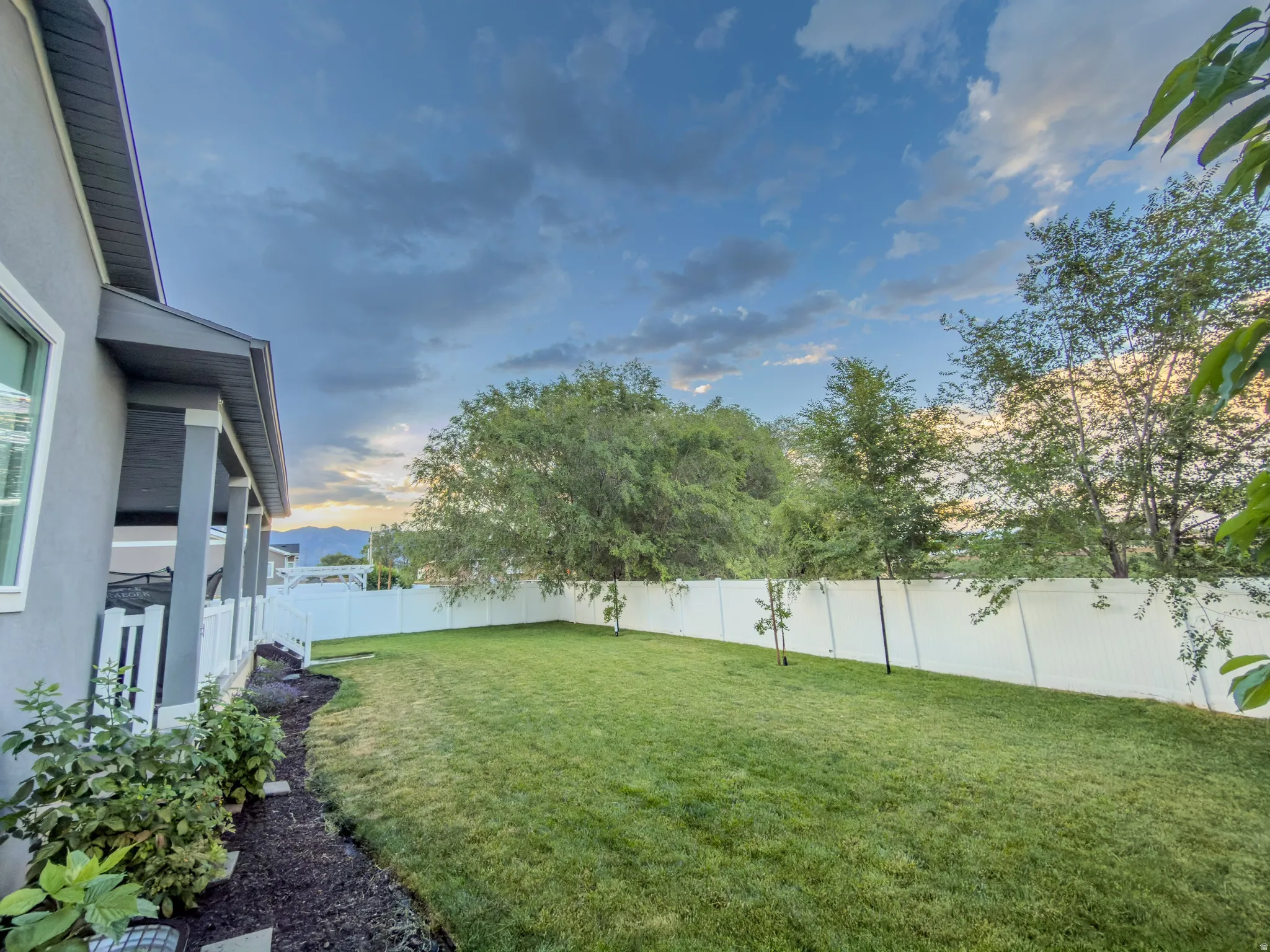 Expansive backyard featuring a manicured lawn, white privacy fencing, and mature perimeter trees