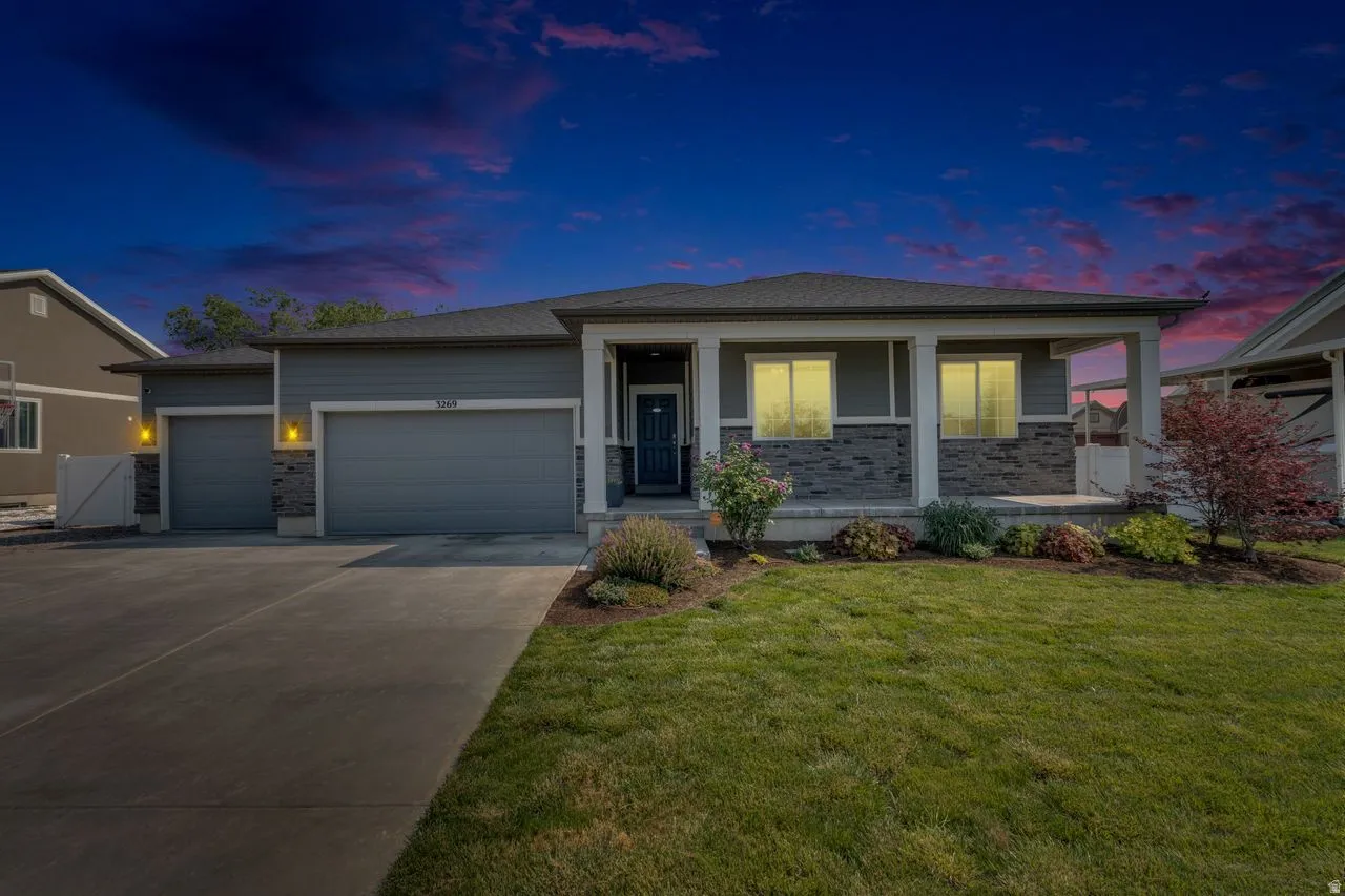 Contemporary ranch-style residence featuring a grey exterior with stone accents, a covered front porch, and an attached two-car garage