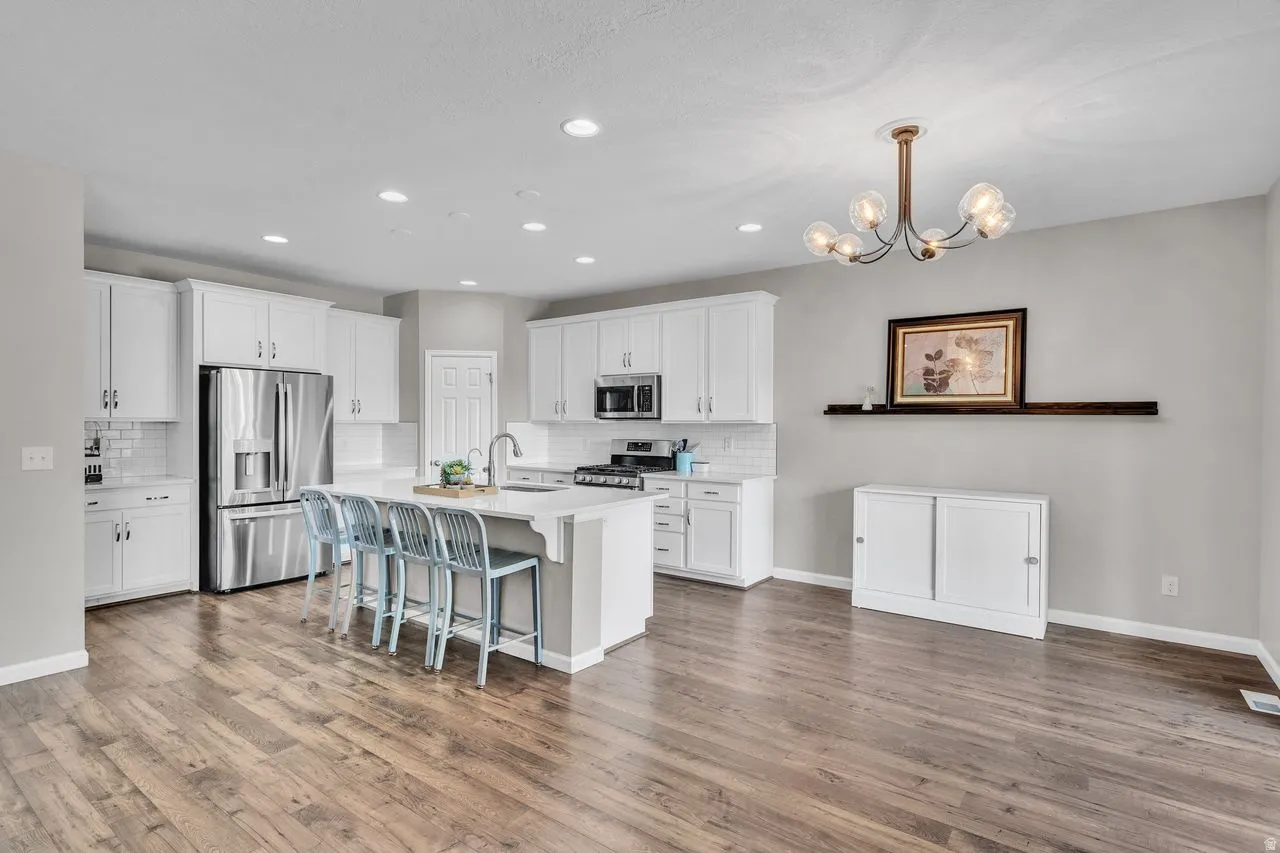 Kitchen featuring a central island with seating, stainless steel appliances, white cabinetry, wood-finish flooring, and recessed lighting