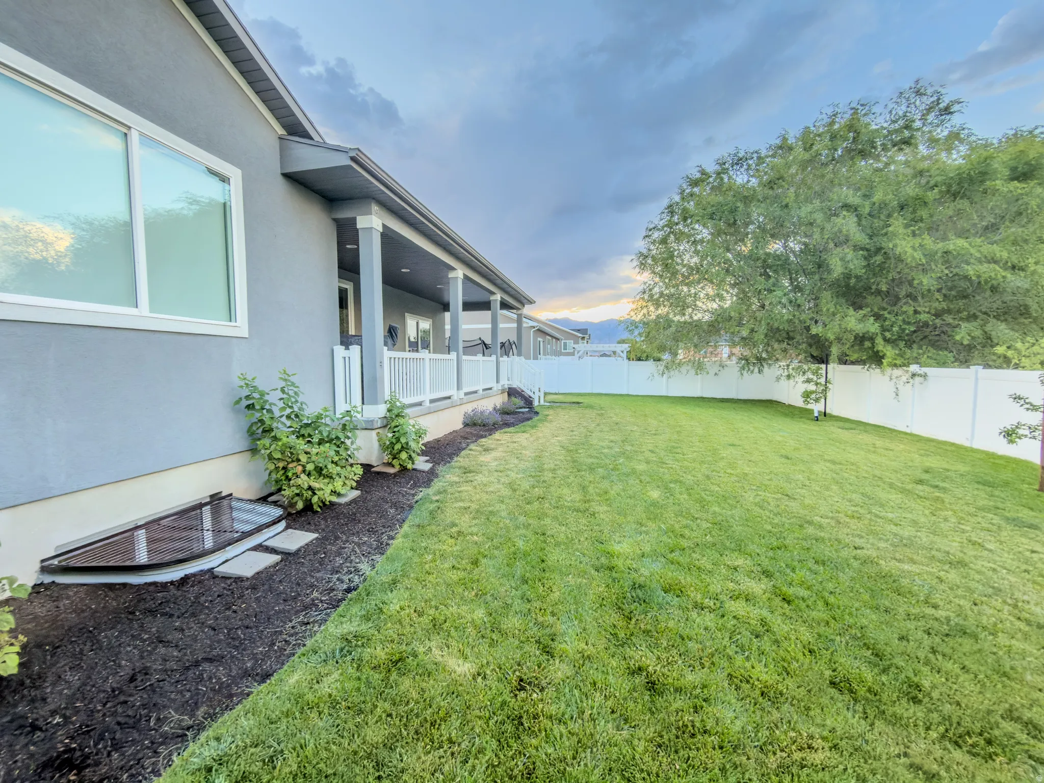 Expansive backyard featuring a manicured lawn, a large mature tree, and a white vinyl privacy fence