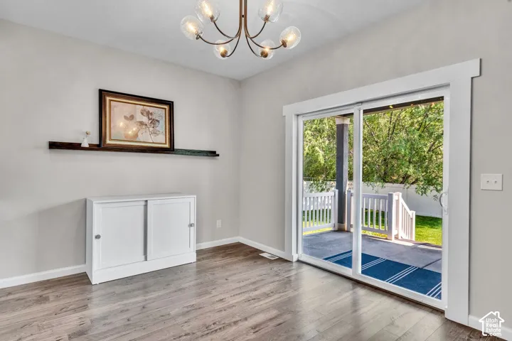 Sliding glass patio door with white trim, wood-finish flooring, and a contemporary chandelier