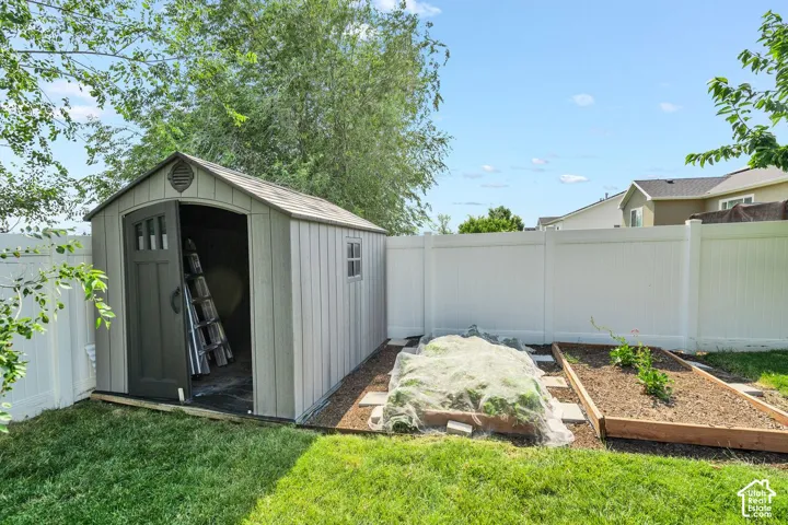 Backyard featuring a shed with a single arched door and side window, white vinyl fencing, and two raised garden beds