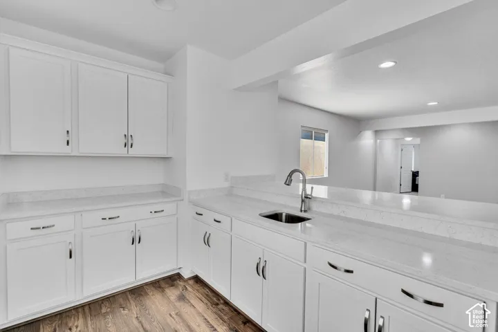 Contemporary kitchen featuring white shaker cabinetry, light-toned countertops, a stainless steel sink with a high-arch faucet, recessed lighting, and wood-finish flooring