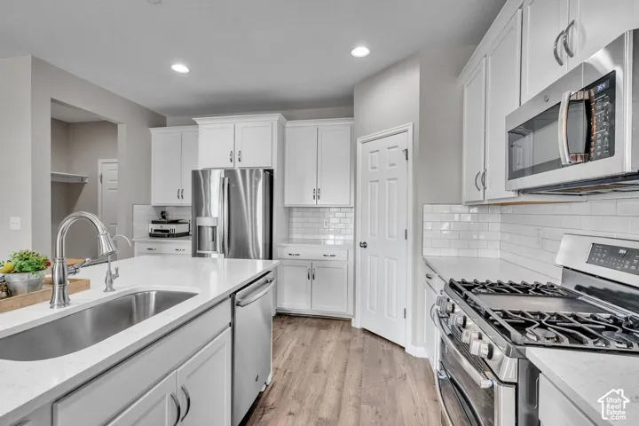 Contemporary kitchen featuring white cabinetry, stainless steel appliances, a gas range, a large kitchen island with an undermount sink, and wood-finish flooring