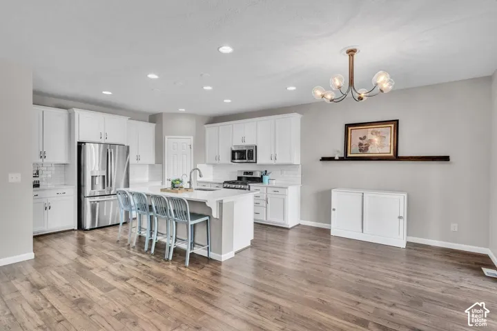 Kitchen featuring a central island with seating, stainless steel appliances, white cabinetry, wood-finish flooring, and recessed lighting