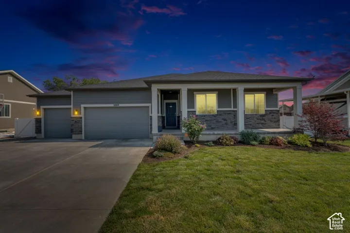 Contemporary ranch-style residence featuring a grey exterior with stone accents, a covered front porch, and an attached two-car garage