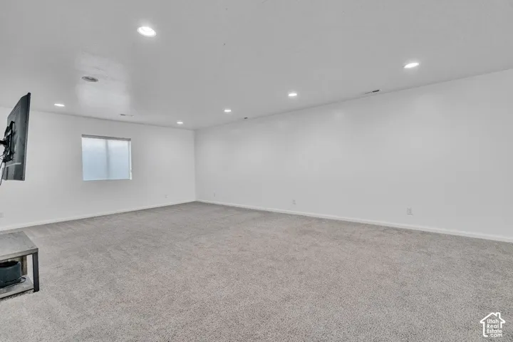Spacious room featuring light gray carpeting, recessed ceiling lighting, a single window with a privacy screen, and white painted walls