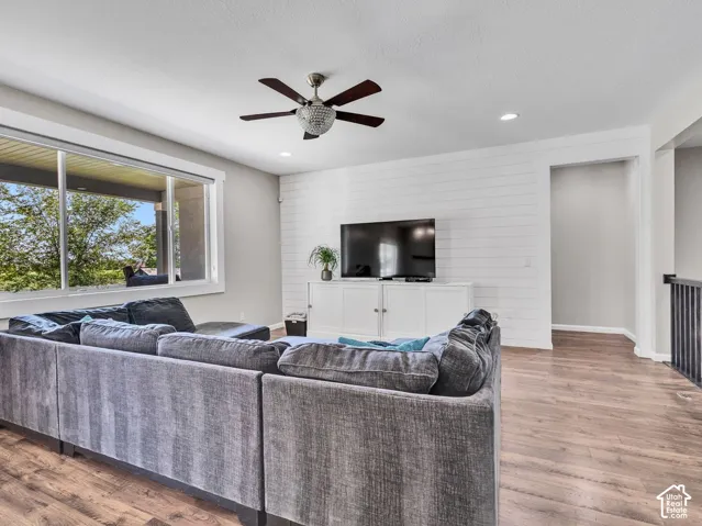 Open-concept living space with wood-finish flooring, a contemporary ceiling fan, recessed lighting, and a shiplap accent wall