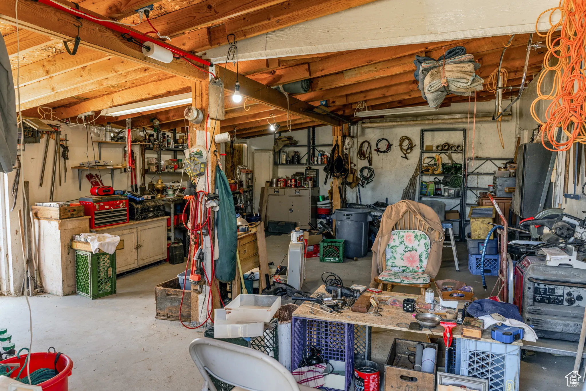 Exposed wood beam ceiling in a utilitarian workspace with concrete flooring, built-in shelving, and a prominent workbench