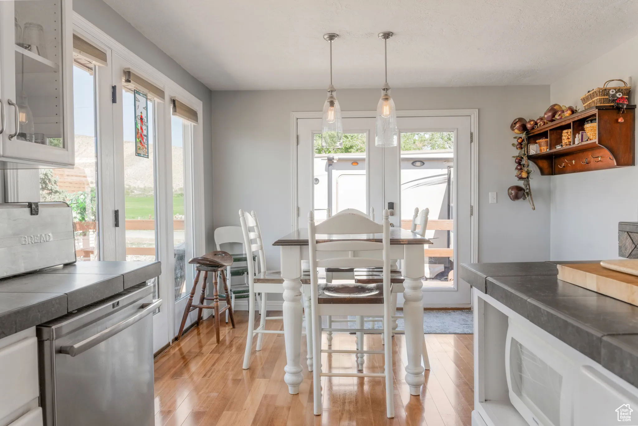 Kitchen featuring hardwood flooring, concrete-finish countertops, stainless steel dishwasher, glass-front cabinetry, and pendant lighting