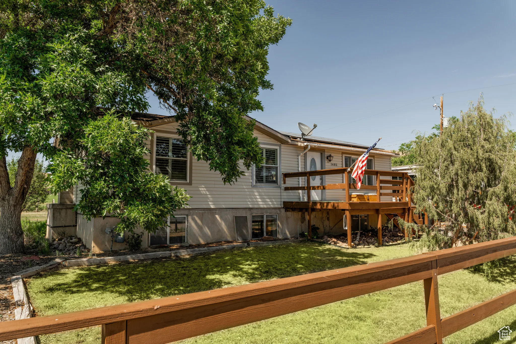 Split-level residence featuring a light-colored siding exterior, an elevated wood deck, and a mature tree providing shade