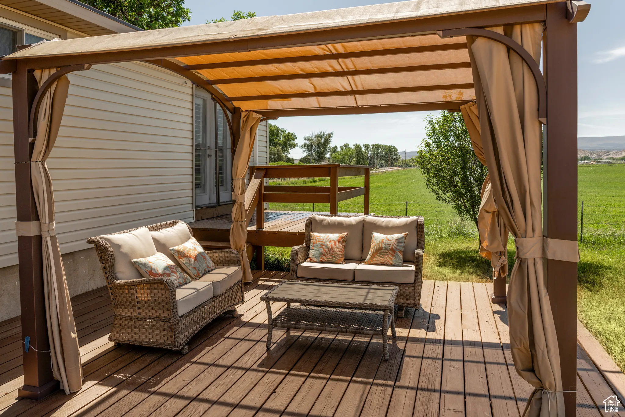 Expansive outdoor deck featuring a covered pergola, light-toned privacy curtains, wood-finish flooring, and direct exterior access