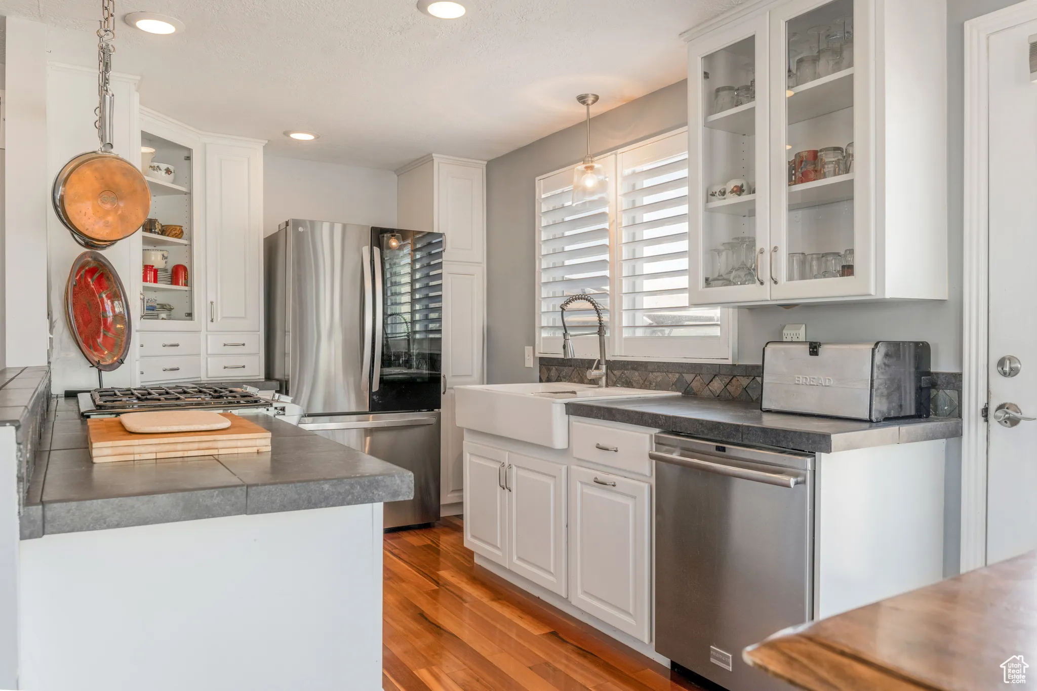 Bright kitchen featuring wood-finish flooring, white cabinetry, stainless steel appliances, a farmhouse sink, and a tiled backsplash