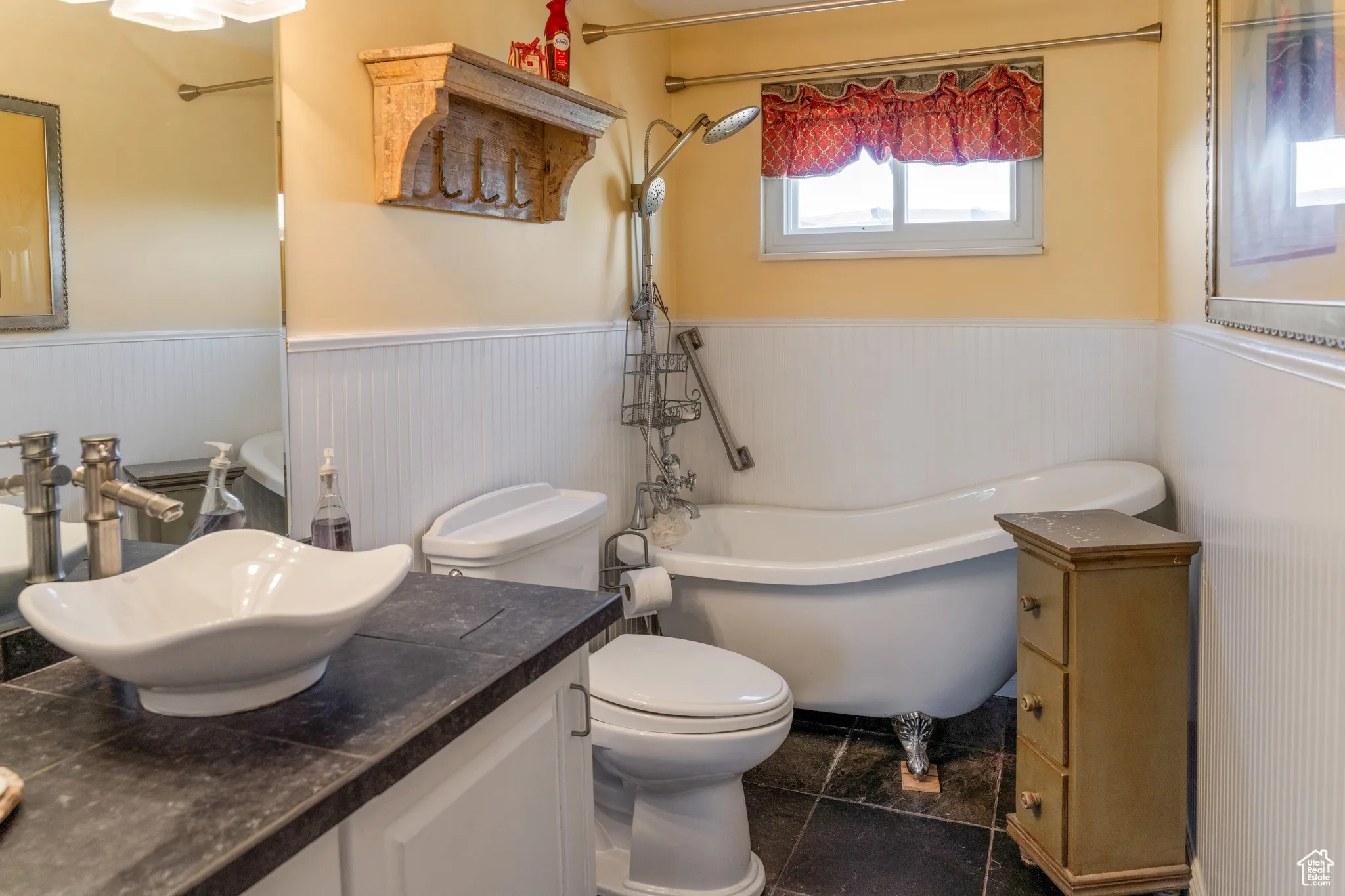Bathroom featuring a freestanding clawfoot tub, white beadboard wainscoting, and dark tile flooring