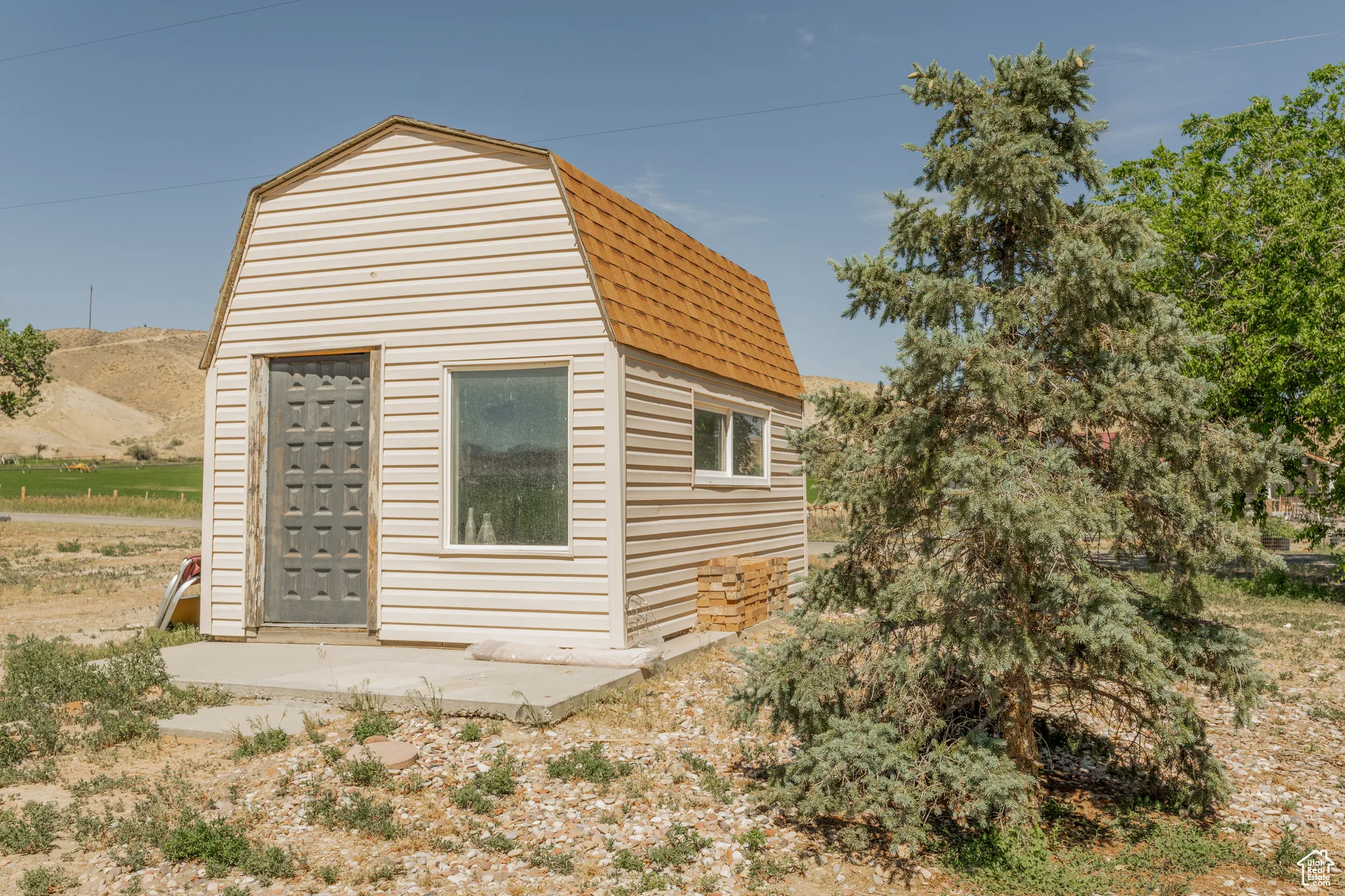 Freestanding barn-style structure with beige horizontal siding and a brown shingle roof