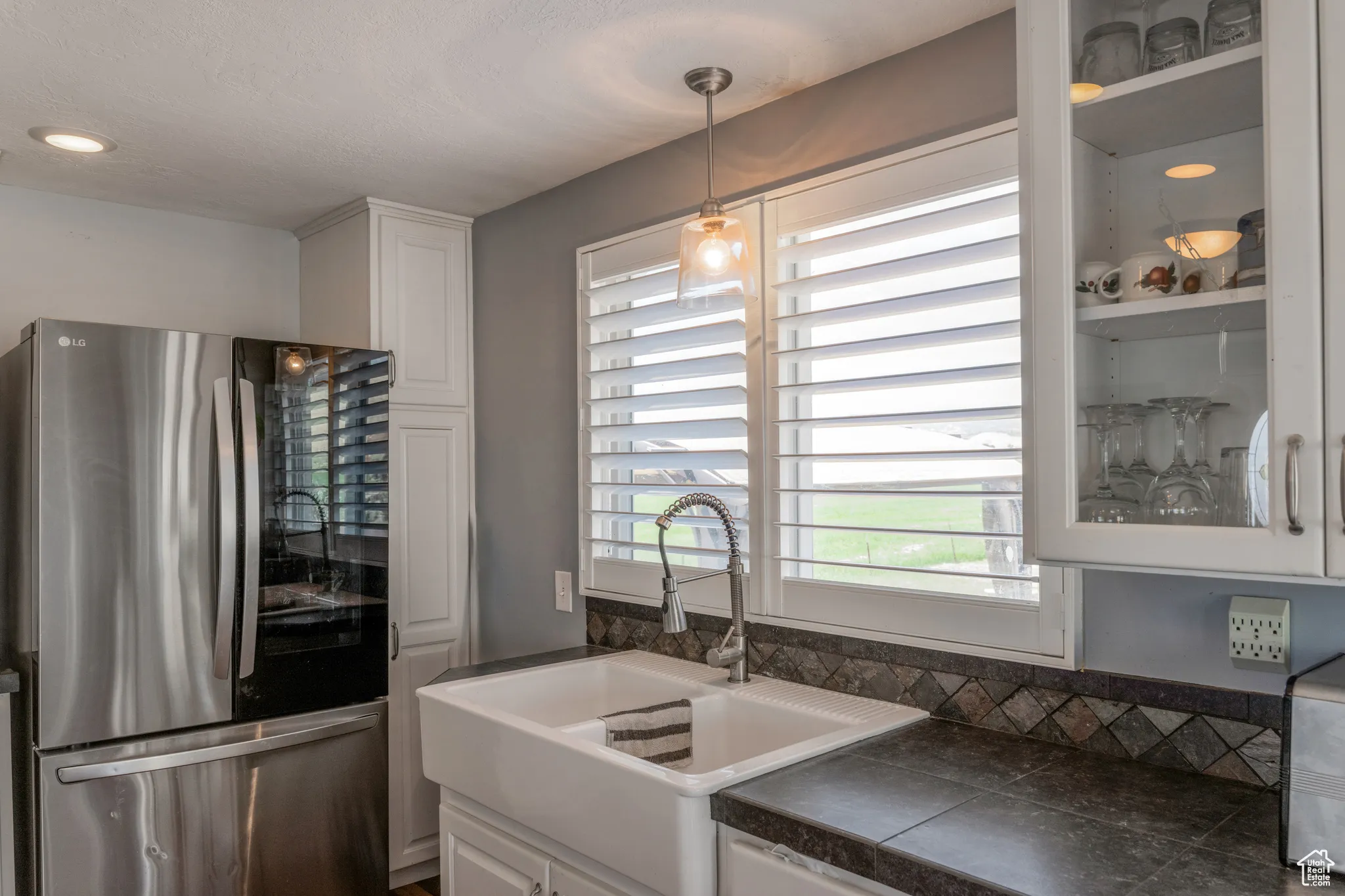 White apron-front sink beneath a window with plantation shutters